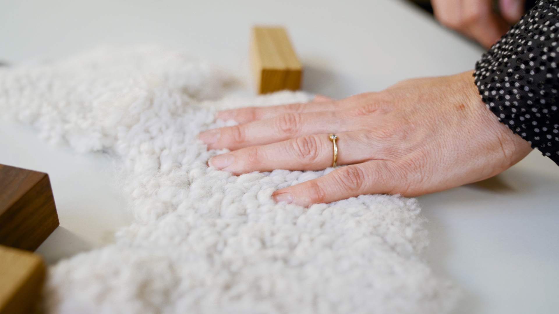 Hand resting on a soft white bouclé textile beside oak and walnut wood samples